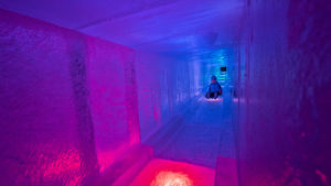 A child is sliding in an ice tunnel, illuminated in blue and red LED. (Ice Castles)