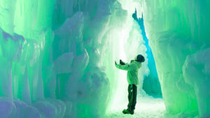 Ice sculptures tower above a child in a green illuminated castle. (Ice Castles)