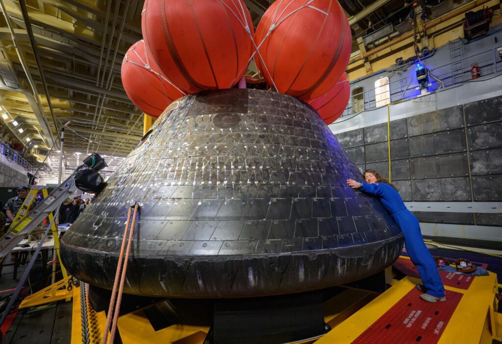 Artemis II astronaut Christina Koch hugs the Orion spacecraft in the well deck of USS John P. Murtha on April 11, one day after the crew splashed down off the coast of California. (Bill Ingalls/NASA via CNN Newsource)